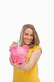 Young blond woman putting money into a piggy-bank 