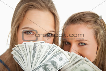 Close-up of two young woman behind dollars