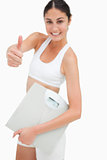 Slim young woman holding a scales the thumb-up