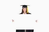A woman in her graduation gown holds a blank sheet in front of h
