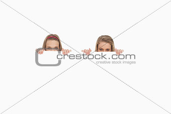Close-up of young women hiding behind a blank sign
