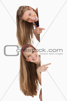 Portrait of two long hair students pointing behind a blank sign