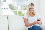 A woman sitting on the couch smiling as she uses her phone