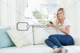 A woman sitting sideways on the couch as she uses her phone and 