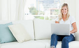 A woman sitting on the couch with a laptop in front of her as sh