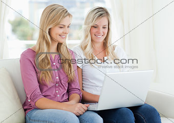 A girl and her friend looking into a laptop while on the couch
