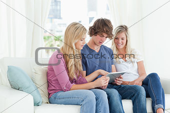 Borther and sisters sit on the couch while looking at a tablet p