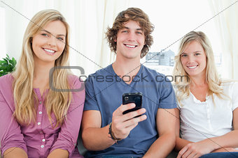 Three friends looking at the camera as the boy has a phone in hi