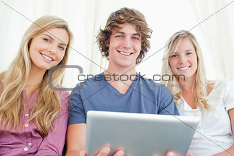 Three friends looking at the camera while holding a tablet