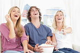 Three friends eating popcorn while laughing at the show