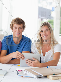 A smiling couple hold a tablet as they both look into the camera