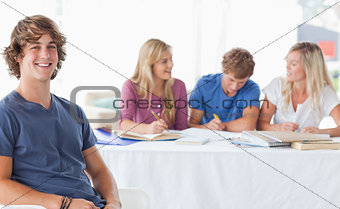 Smiling man sitting on front of his friends and looking at the c
