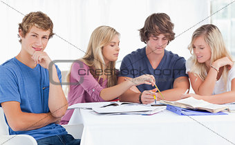 Four friends studying as one guy looks at the camera and smiles