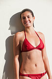 Smiling woman in bikini leaning against a wall