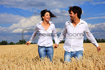 Happy couple running in a field smiling and holding hands
