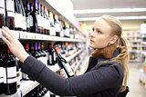Young woman is choosing wine in the supermarket.