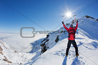 Mountaineer reaches the top of a snowy mountain in a sunny winter day.
