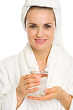 Young woman in bathrobe holding glass of water