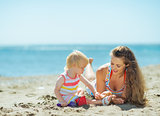 Mother and baby girl playing with sand on beach