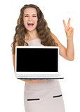 Happy young woman showing laptop and victory gesture