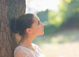 Thoughtful girl leaning on tree and looking on copy space
