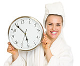 Happy young woman in bathrobe holding clock