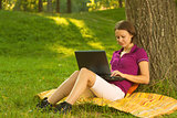 Beautiful young brunette working on a laptop in the park
