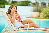 Happy young woman laying on sunbed and drinking cocktail