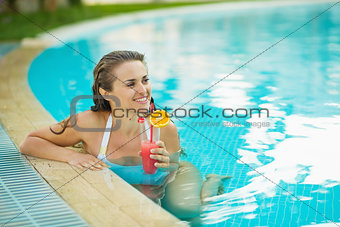 Happy young woman at pool with cocktail looking on copy space