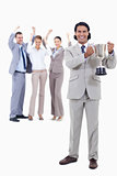 Businessman smiling and holding a cup with people cheering behin