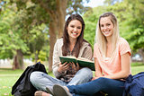 Smiling teenagers sitting while studying with a textbook