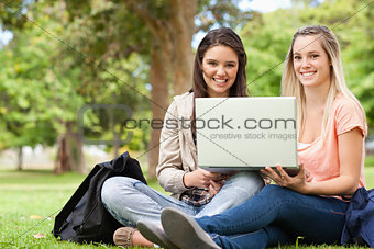 Smiling teenagers sitting while using a laptop