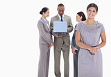 Woman welcoming and co-workers with a laptop in the background