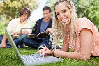 Portrait of a girl using a laptop while lying in a park