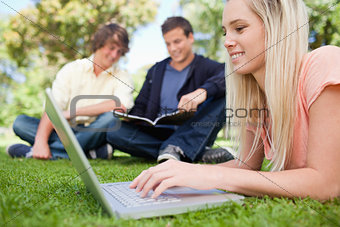 Girl using a laptop while lying in a park