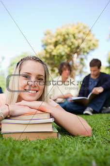 Close-up of a girl lying head on her books in a park