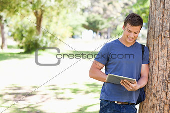 Student leaning against a tree while using a touch pad