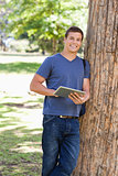 Portrait of a student leaning against a tree while using a touch