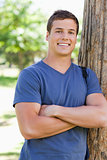 Close-up of a smiling young man leaning against a tree