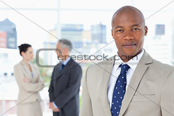 Young executive in a suit standing upright while his team is beh