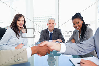 Three smiling co-workers looking at two business people shaking 