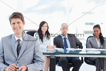 Smiling young businessman sitting in front of his team and looki