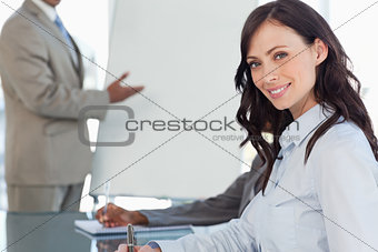 Young smiling businesswoman writing in a notebook during a prese