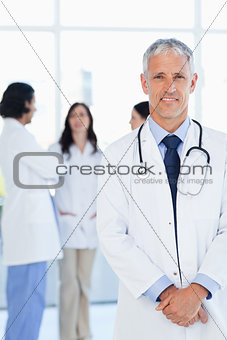 Doctor smiling while his team is communicating in the background