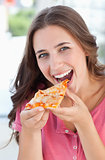 A woman about to eat a piece of pizza as she looks at the camera