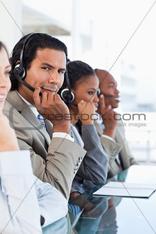 Young call centre employee surrounded by his business team