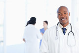 Young doctor standing in a bright room with his team in the back