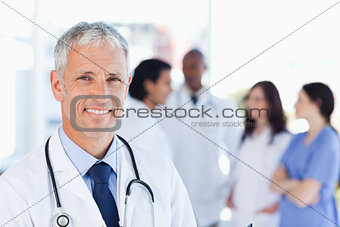 Mature doctor standing upright while waiting for his team