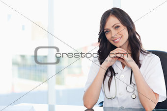 Young nurse sitting at the desk with her hands crossed and leani