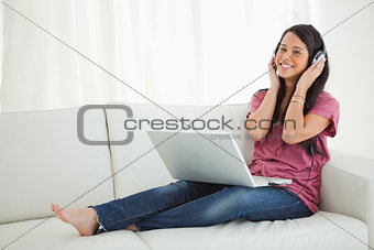 Smiling Latino student enjoying music on her sofa
